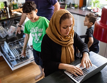 Image of a busy kitchen with children and a woman on her laptop
