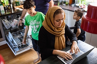 Image of a busy kitchen with children and a woman on her laptop