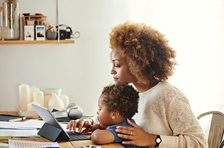 Image of a mother with a baby on her knee looking at her laptop