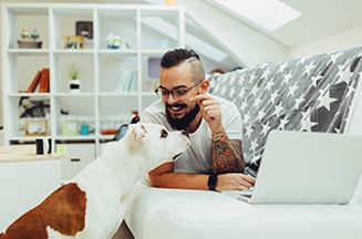 Image of a man working on his laptop with a dog at his side