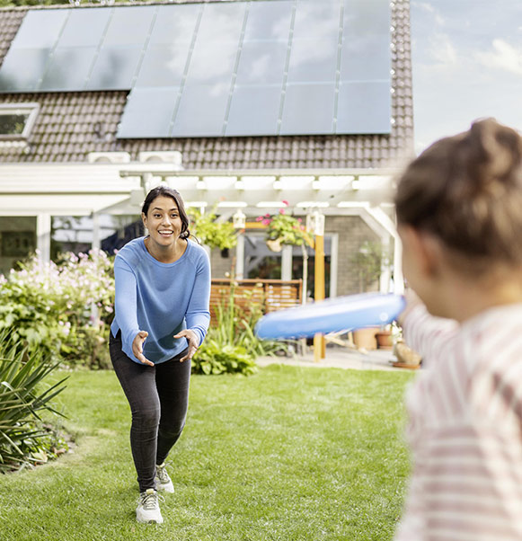 Woman playing with daughter in garden, with Solar panels on roof of house