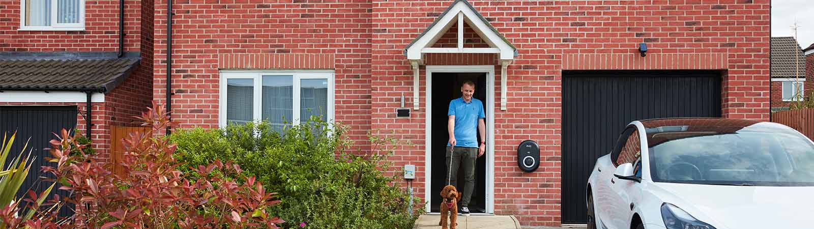 Image of a man at his door with his dog with an EV charger on the front of his house