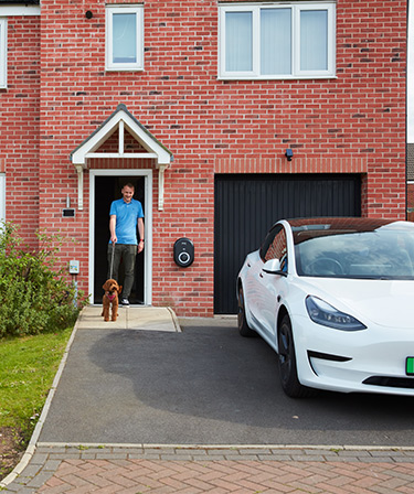 Image of a man at his door with his dog with an EV charger on the front of his house